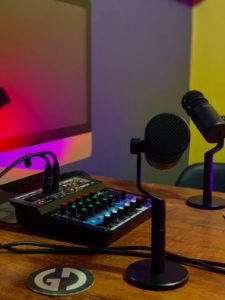 mesa com uma tela de computador, mesa de configuração de áudio e dois microfones